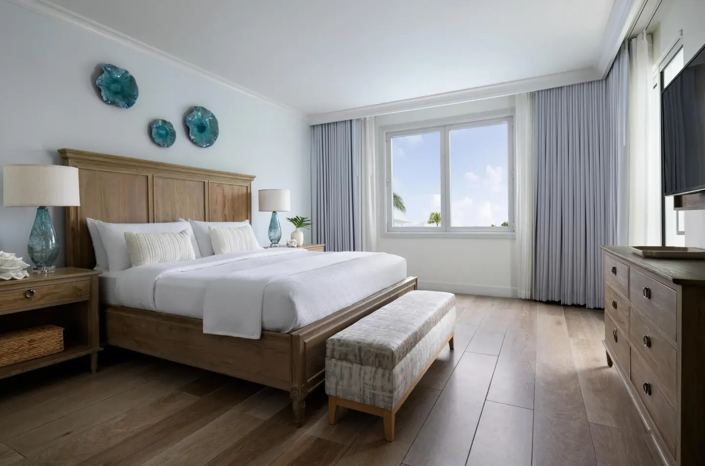 A king bed, dresser, and window in a bright guest room at Sandals Royal Bahamian.