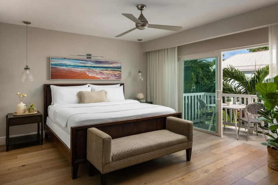 Guest room at Sandals Royal Bahamian with a king bed, sofa bench, ceiling fan, and balcony.