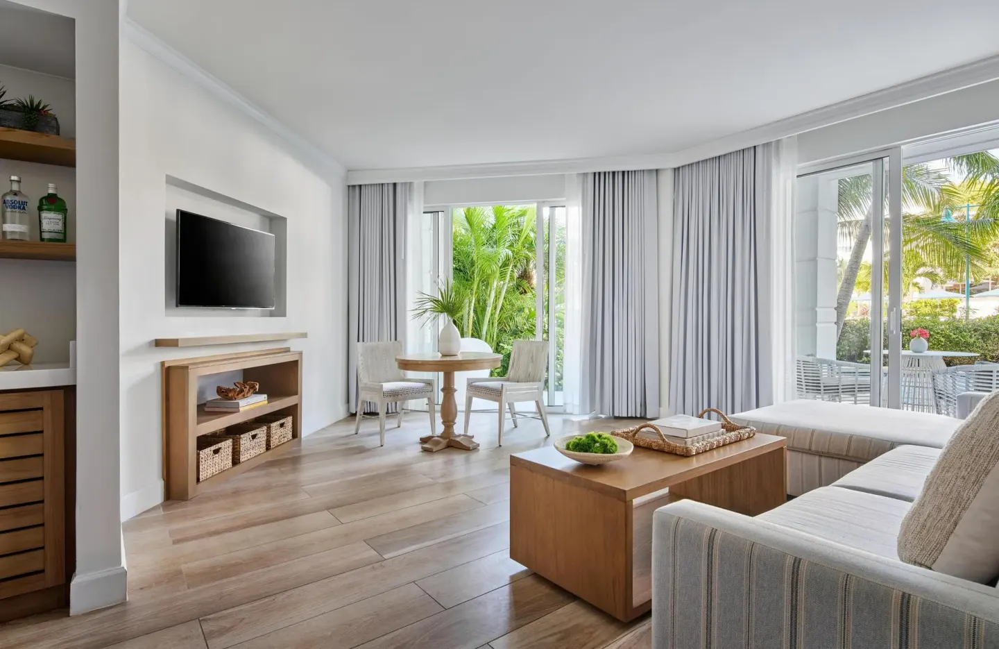 Guest suite living room with sofa, TV, dining nook, and patio at Sandals Royal Bahamian.