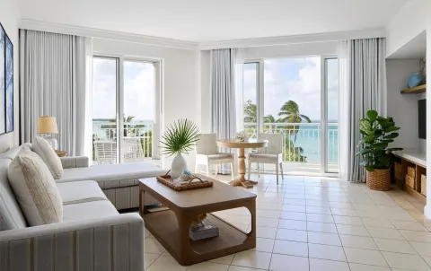 Ocean-view living room with sofa, dining table, and balcony doors at Sandals Royal Bahamian.