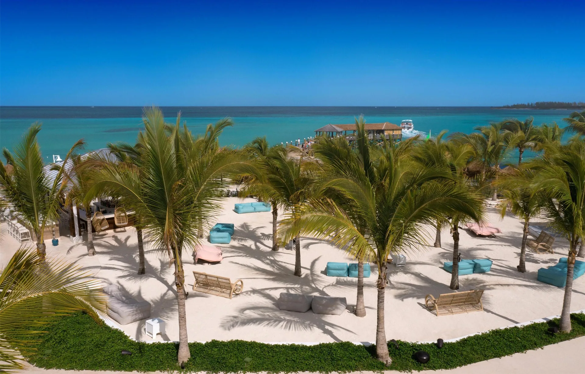 A palm-lined sandy lounge area overlooks the pier and turquoise sea at Sandals Royal Bahamian.