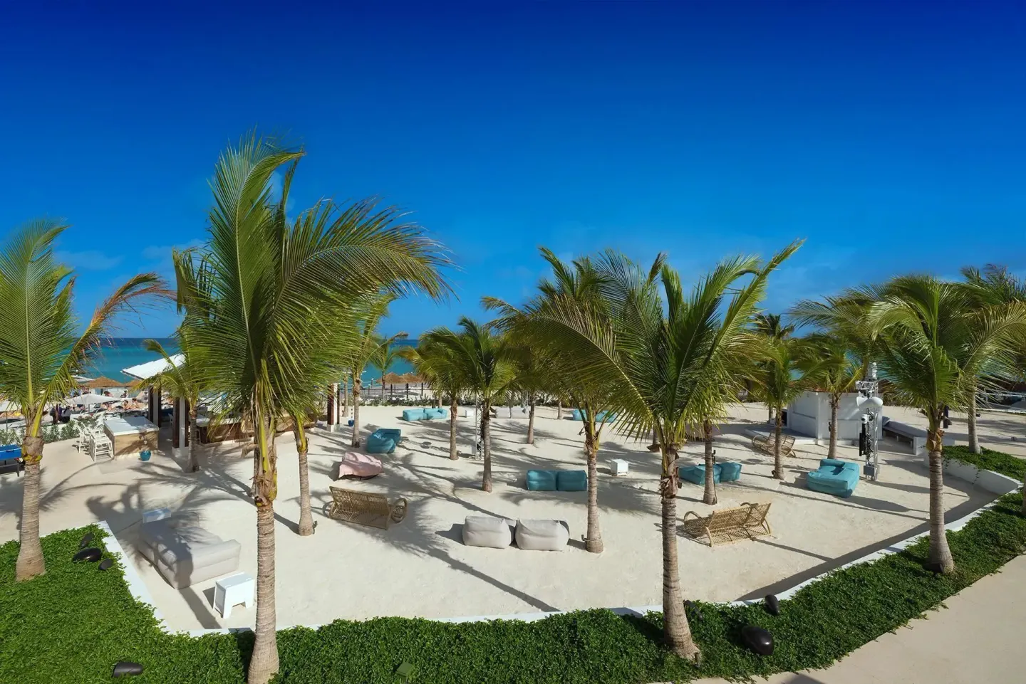Palm trees shade lounge seating on a sandy beachfront terrace at Sandals Royal Bahamian.