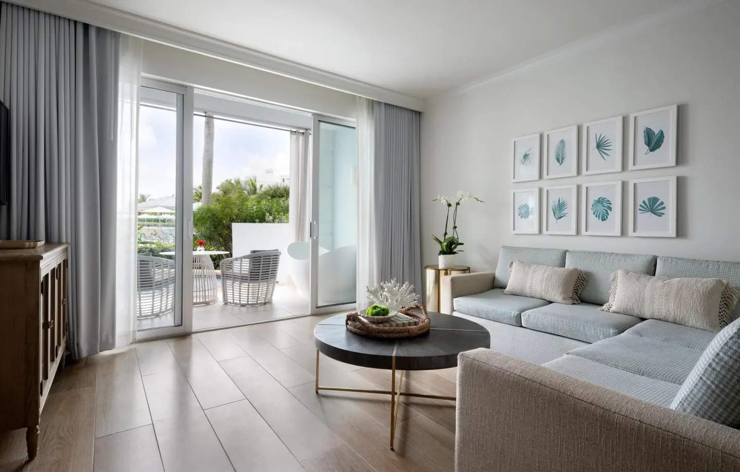 A modern suite living area with patio doors and a gray sectional at Sandals Royal Bahamian.