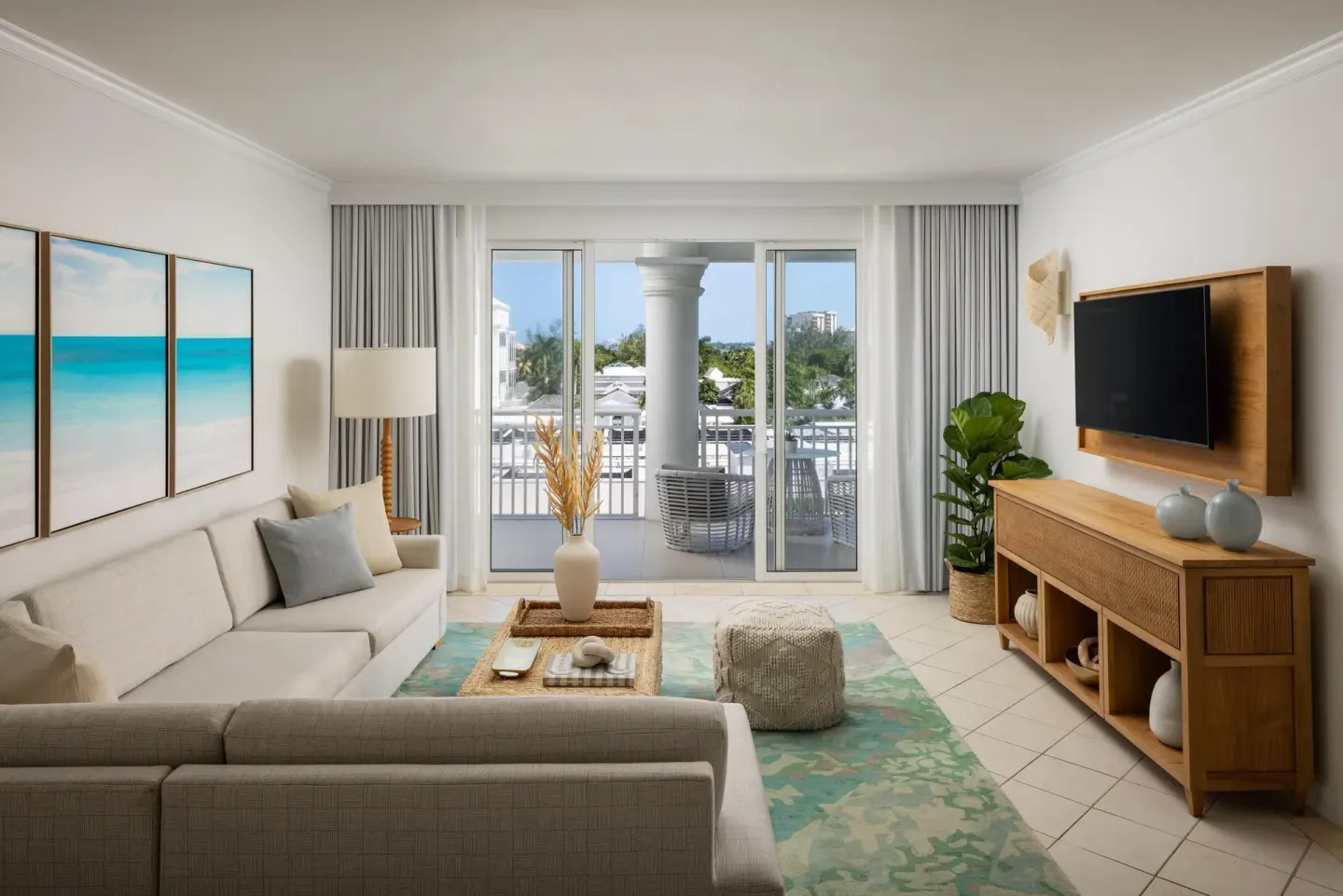 A suite living room with balcony doors and a wall-mounted TV at Sandals Royal Bahamian.