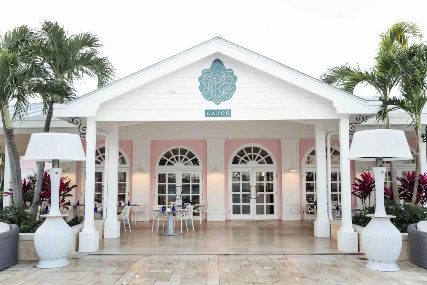 The Kanoo entrance with arched doors, palms, and patio tables at Sandals Royal Bahamian.