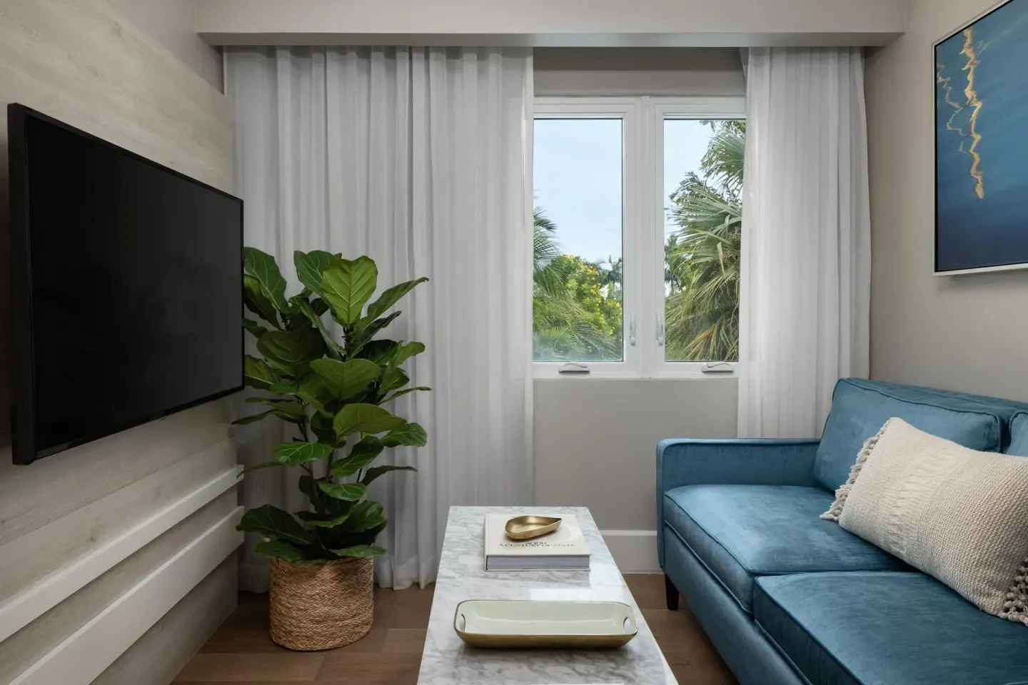 Living area with blue sofa and garden-view window in a villa suite at Sandals Royal Bahamian.