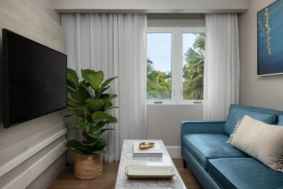 Living area with blue sofa and garden-view window in a villa suite at Sandals Royal Bahamian.