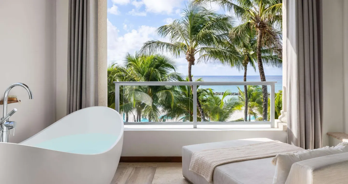 Balcony soaking tub and daybed with palm-framed ocean view at Sandals Royal Barbados.