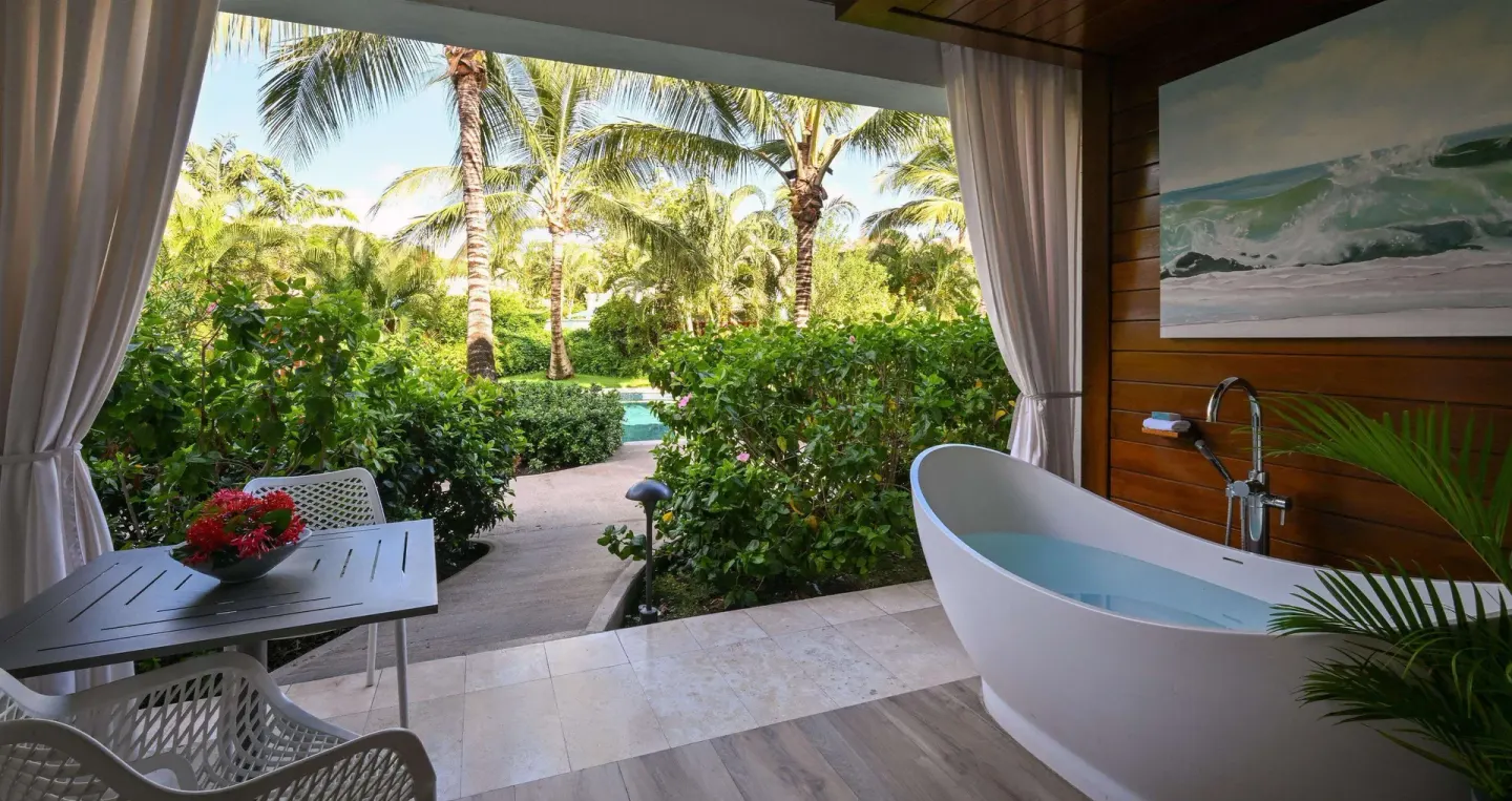 Covered patio with soaking tub, dining table, and tropical garden at Sandals Royal Barbados.