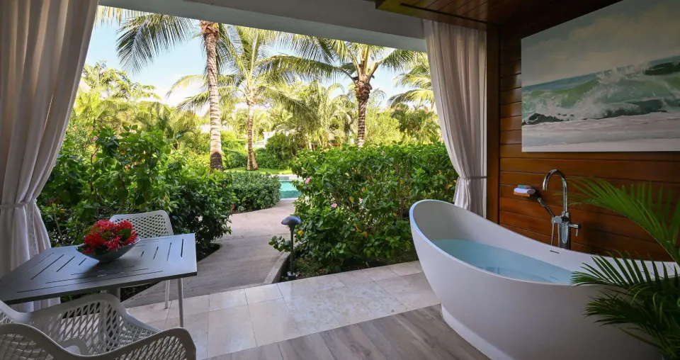 Covered patio with soaking tub, dining table, and tropical garden at Sandals Royal Barbados.
