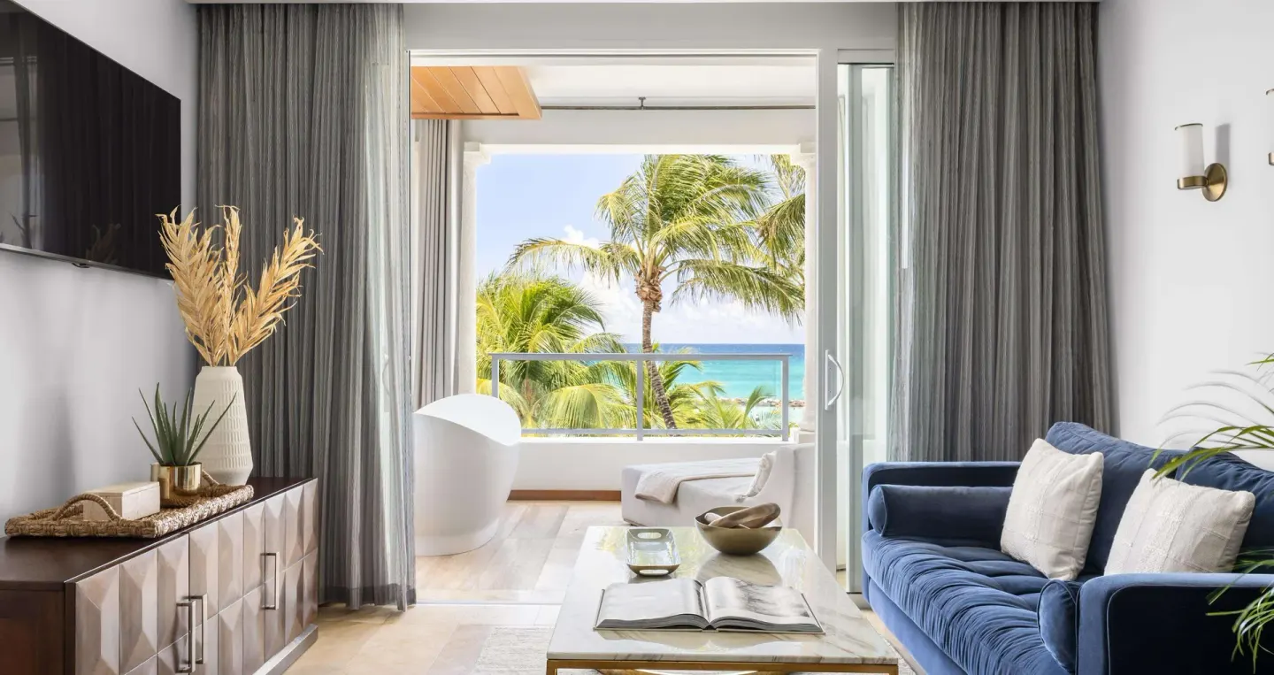 Living area with blue sofa and balcony soaking tub view at Sandals Royal Barbados.