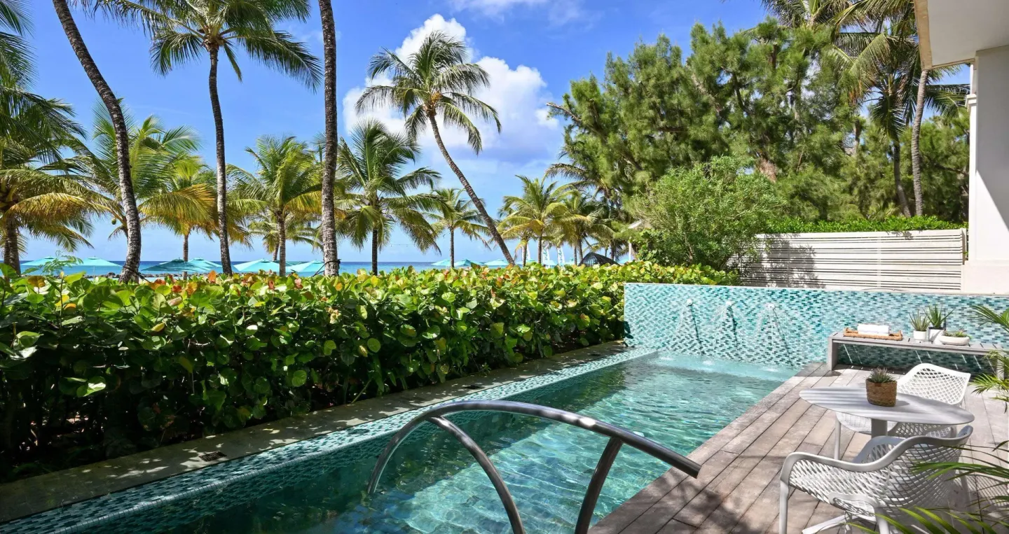 Swim-up patio with pool, loungers, palms and ocean beyond at Sandals Royal Barbados.
