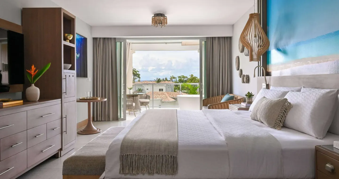 King bedroom in a Club Suite at Sandals Royal Barbados with balcony doors open to a tropical view.