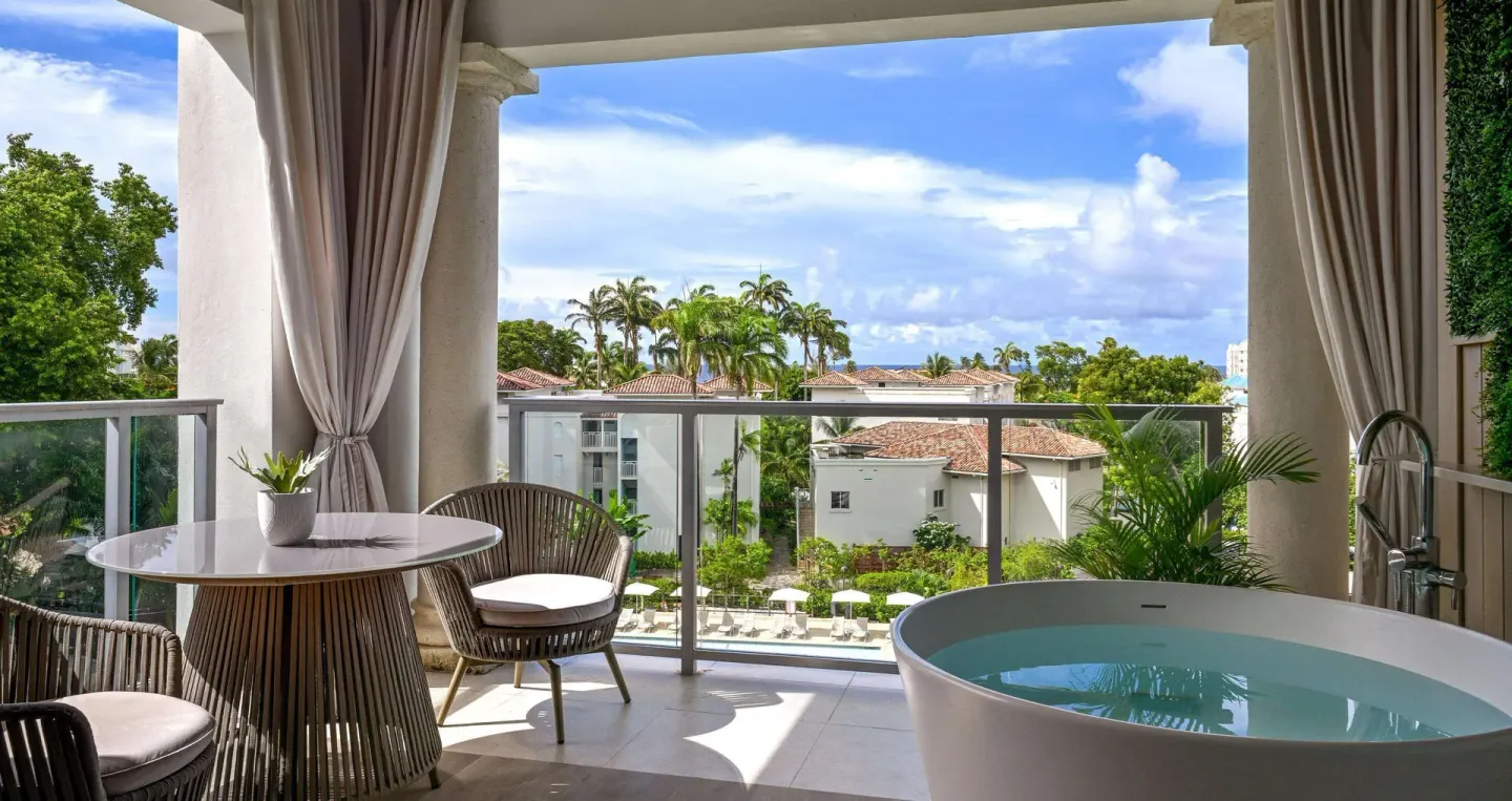 Furnished balcony at Sandals Royal Barbados with soaking tub, table, chairs, and tropical resort view.