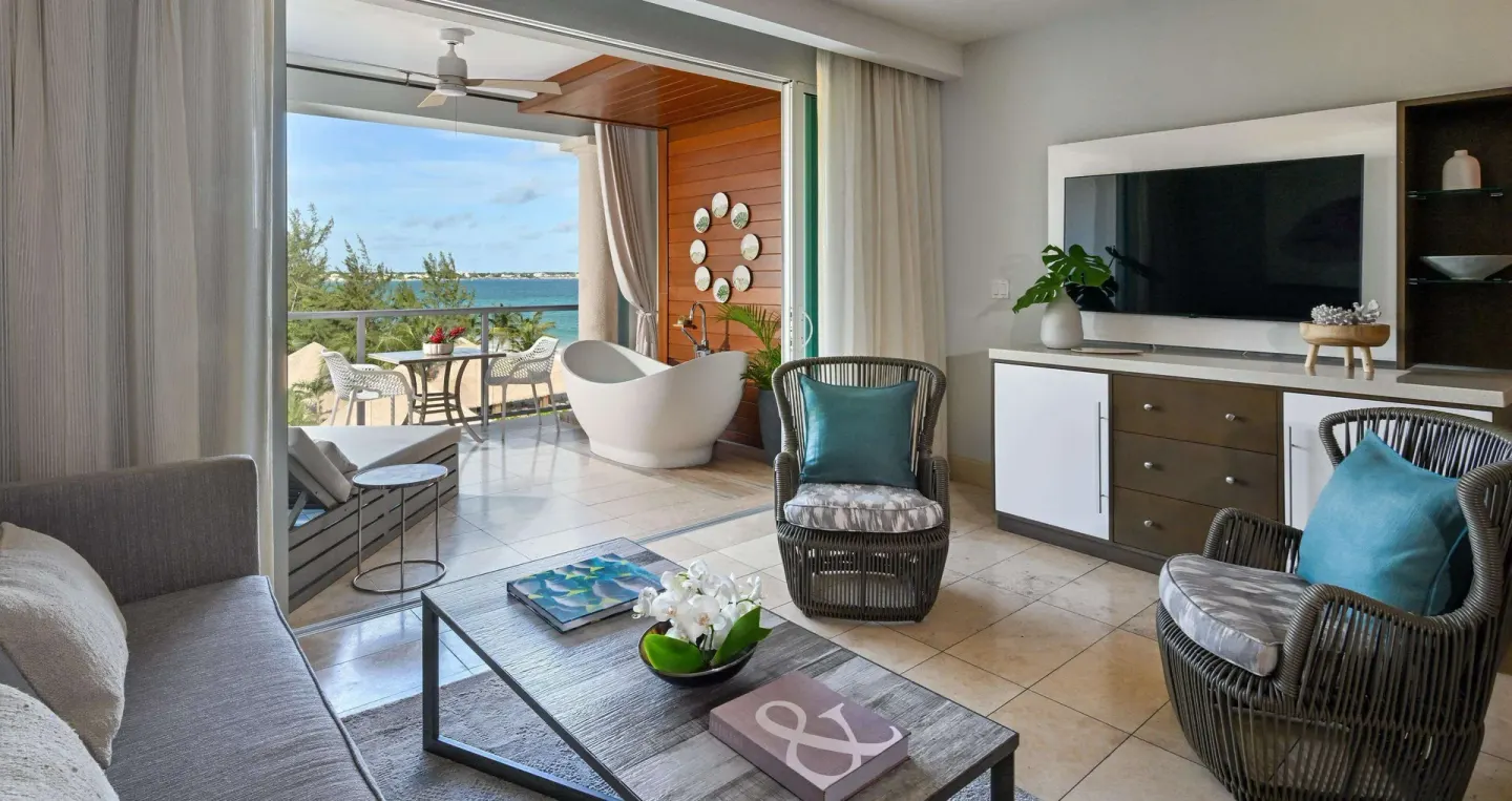 Living area with TV, seating, balcony, and soaking tub at Sandals Royal Barbados.