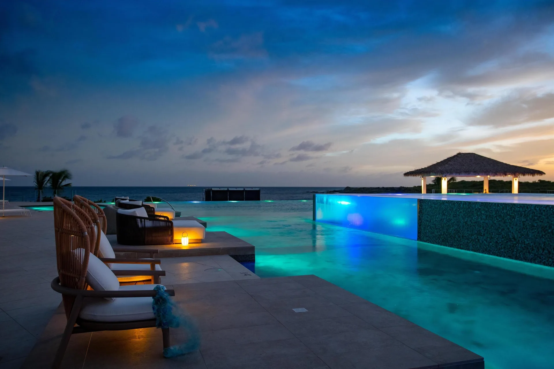 Evening pool deck with glowing water and lounge chairs at Sandals Royal Curacao.