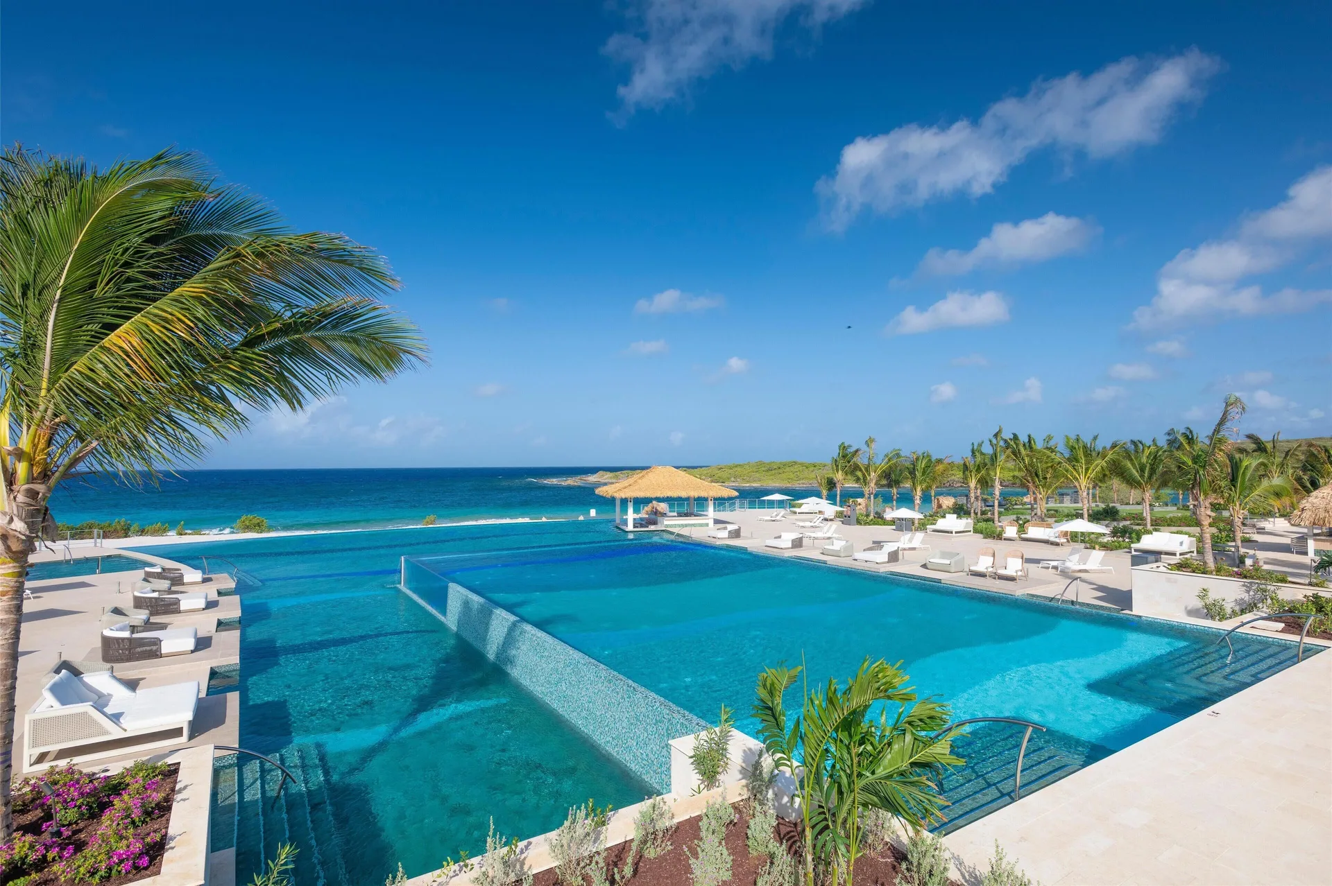 Infinity pool with ocean view and white loungers at Sandals Royal Curacao.