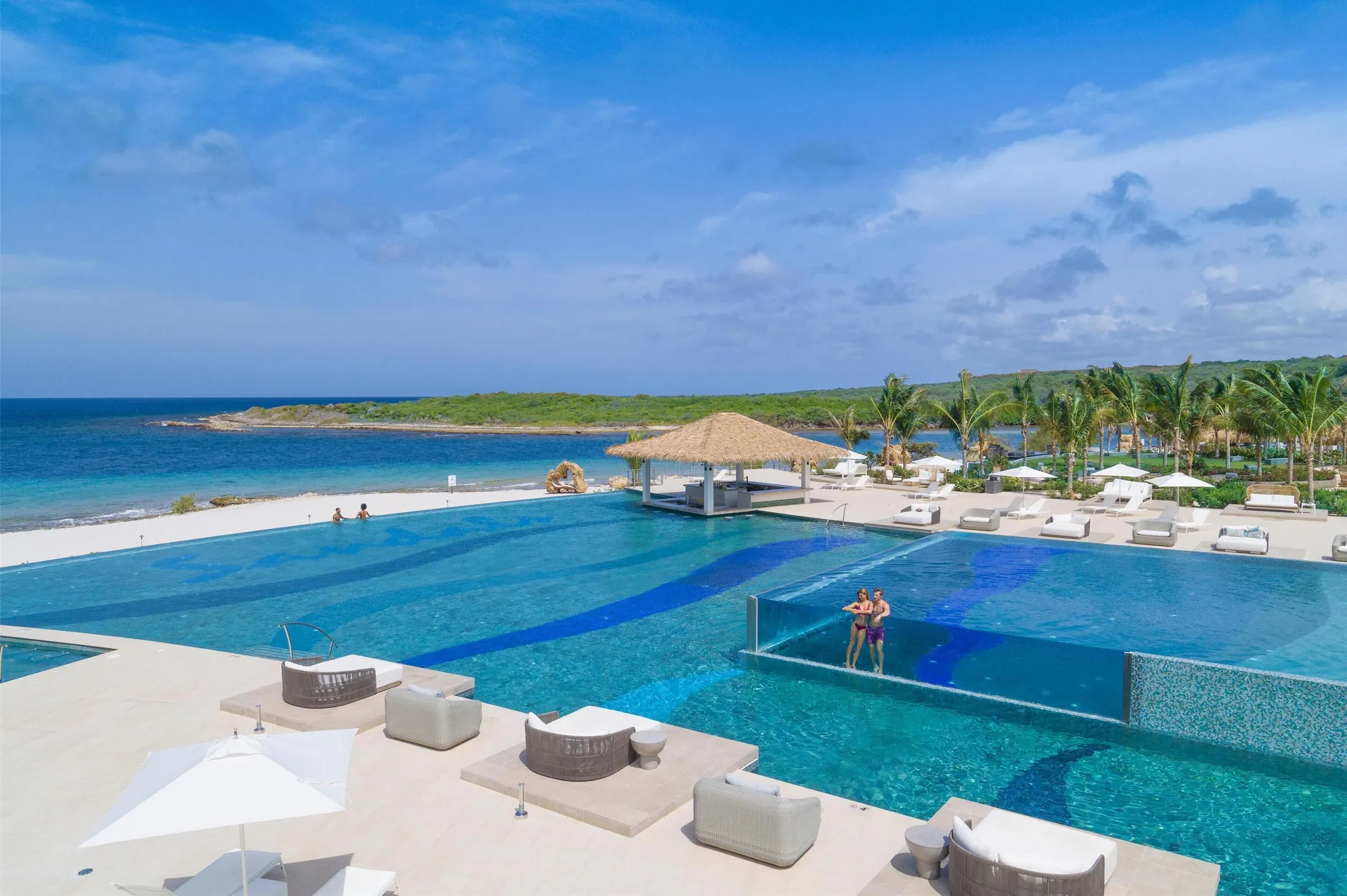 Oceanfront infinity pool with loungers and a thatched pavilion at Sandals Royal Curacao.