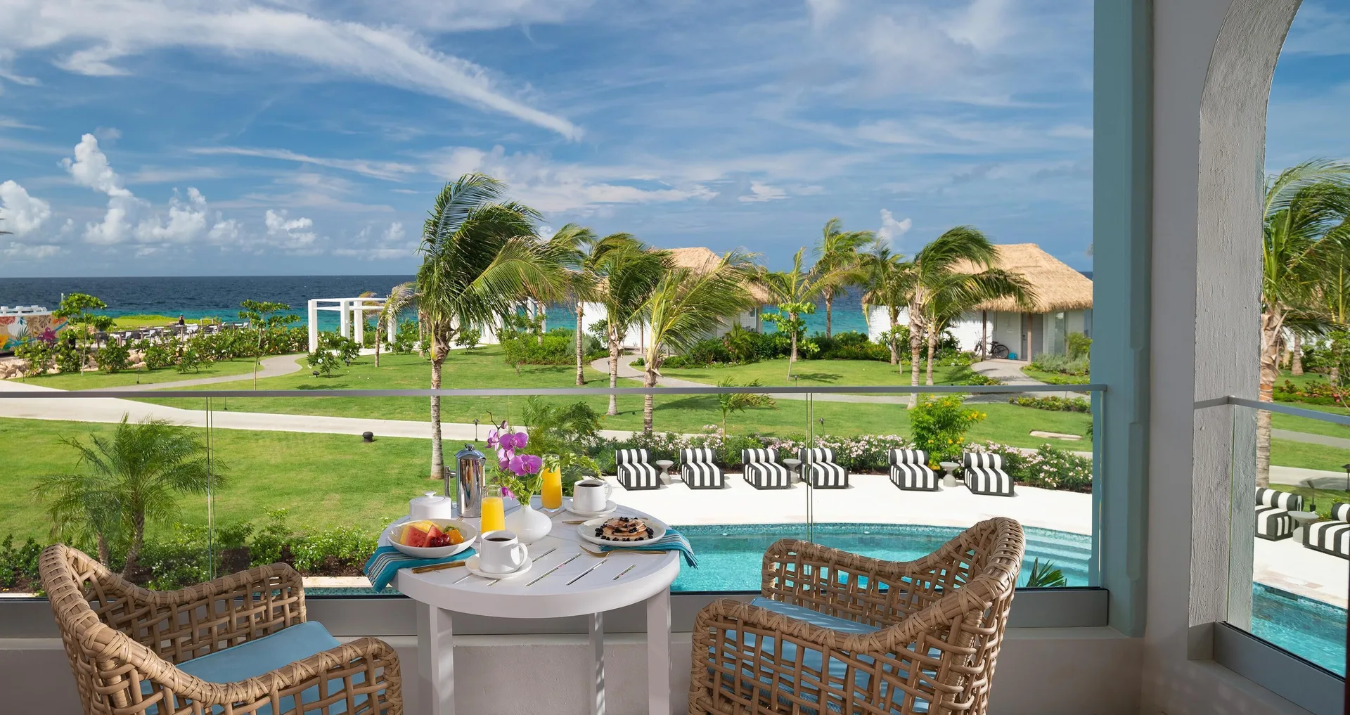 Balcony breakfast setup overlooking pool, lawns, and ocean at Sandals Royal Curacao.