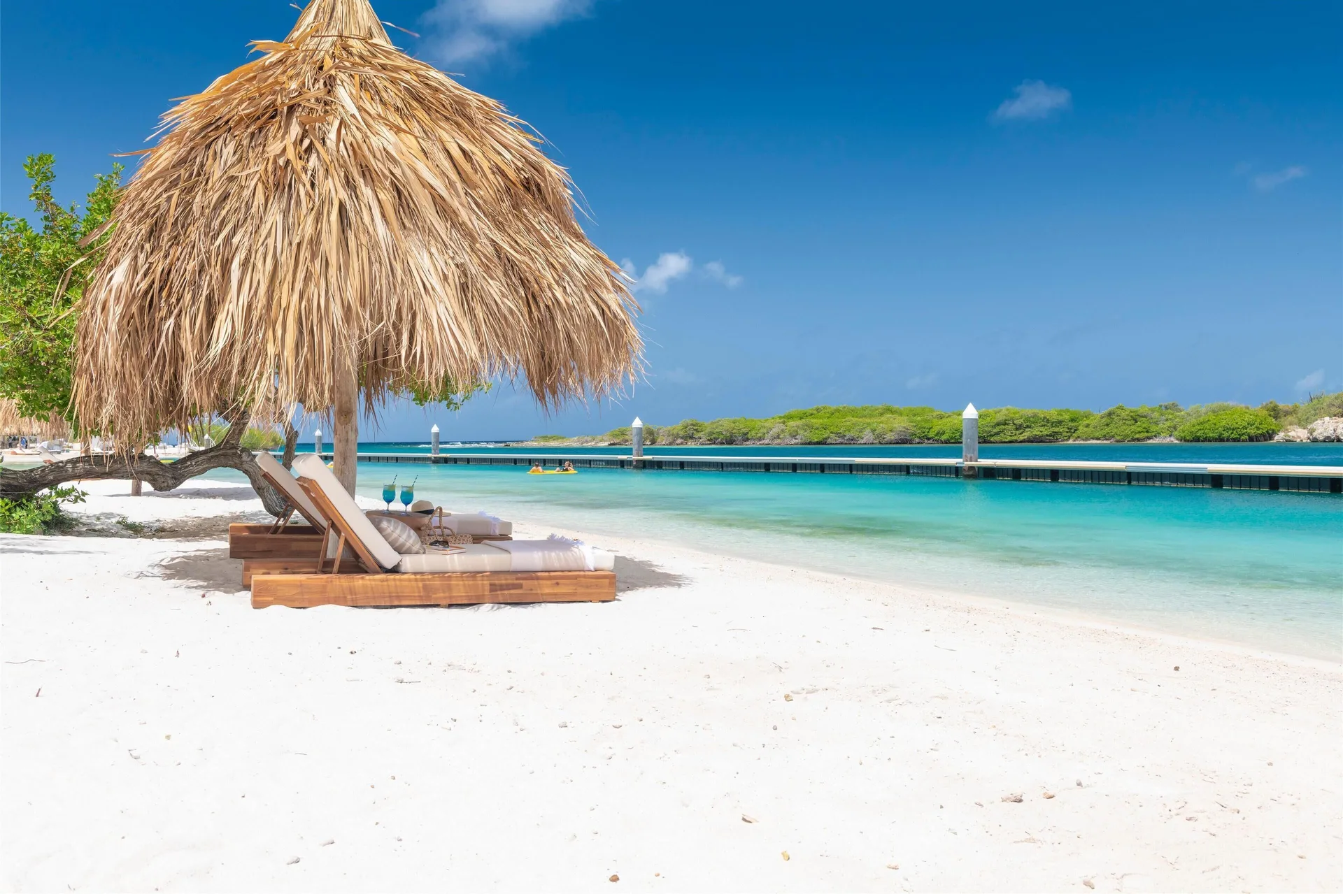 Thatched palapa with lounge chairs beside calm turquoise water at Sandals Royal Curacao.
