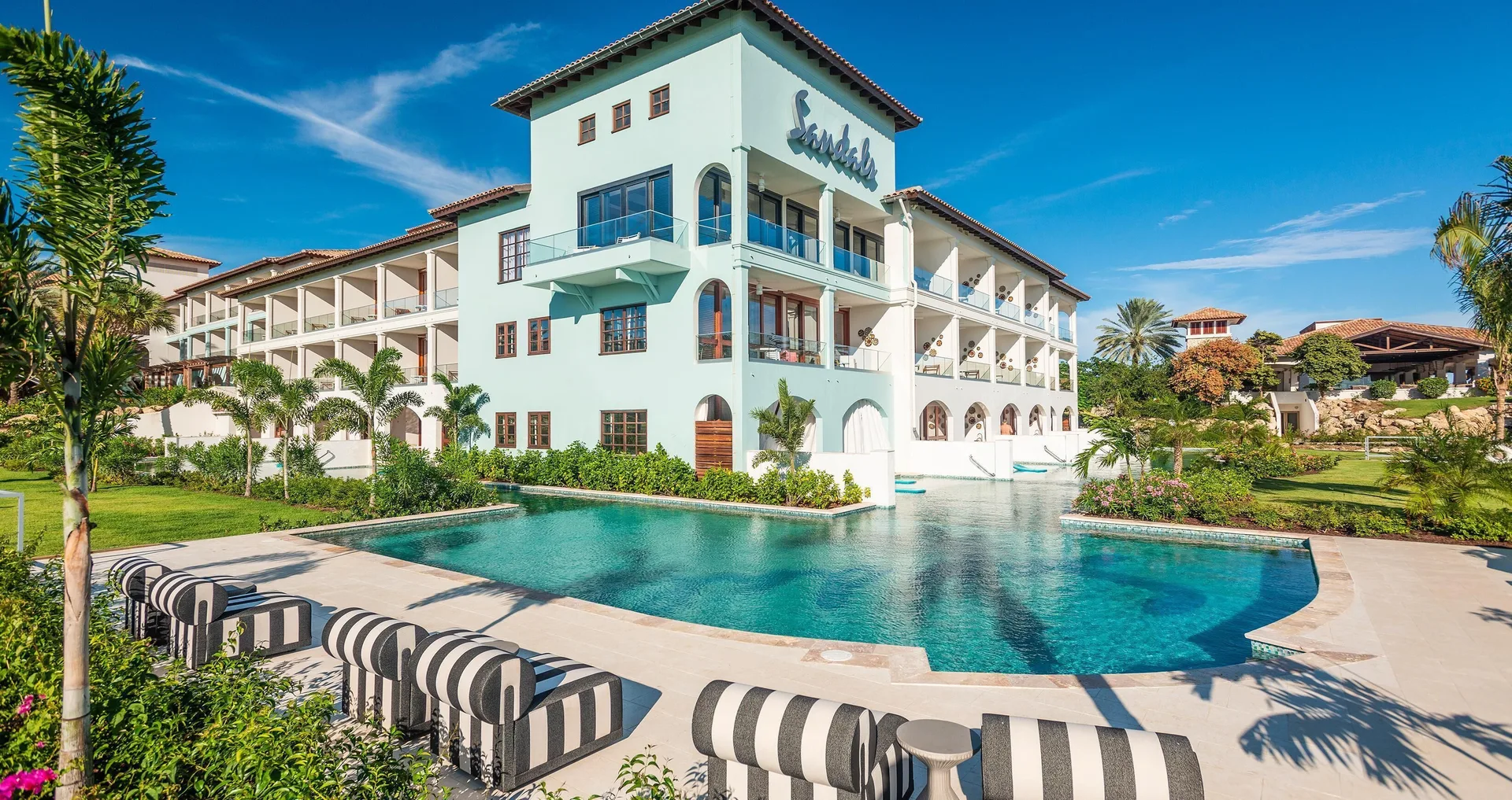 Resort building and pool with striped loungers at Sandals Royal Curacao.