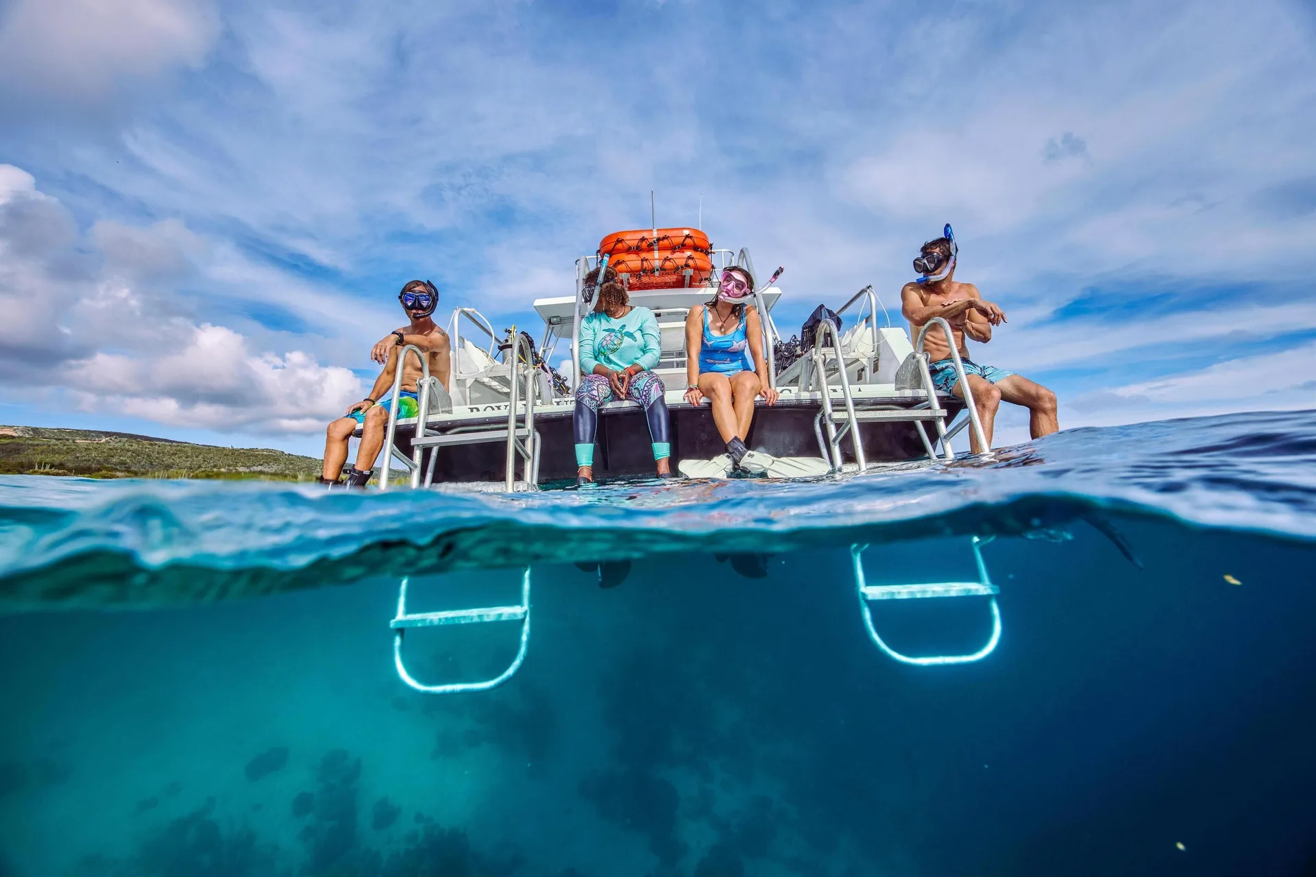 Snorkelers sit on a boat ladder above clear water near Sandals Royal Curacao.