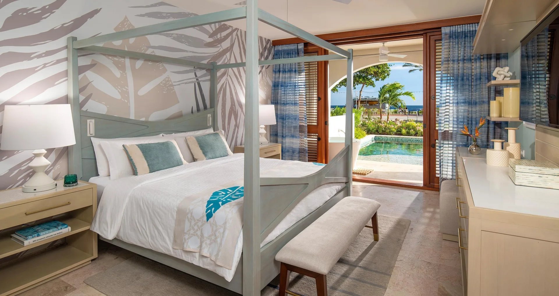 Canopy king bed beside glass doors to a swim-up pool at Sandals Royal Curacao.