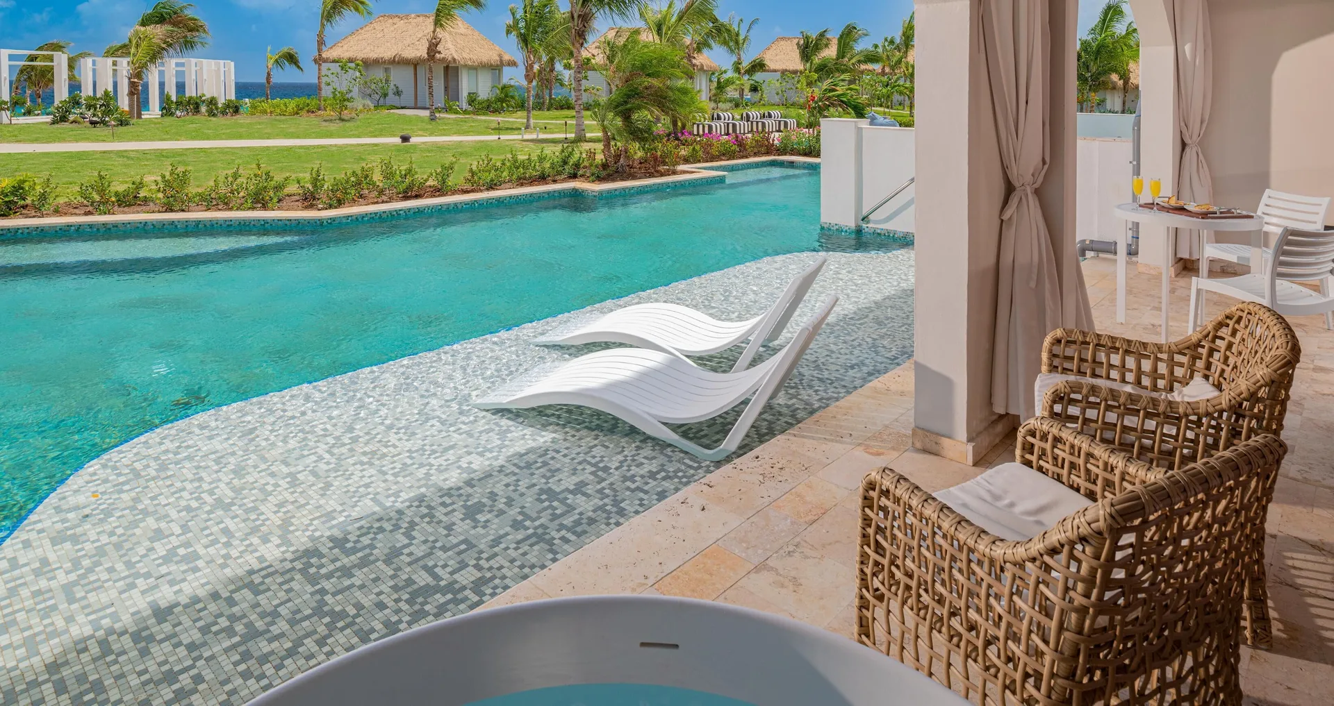 Swim-up terrace with loungers and wicker chairs at Sandals Royal Curacao.