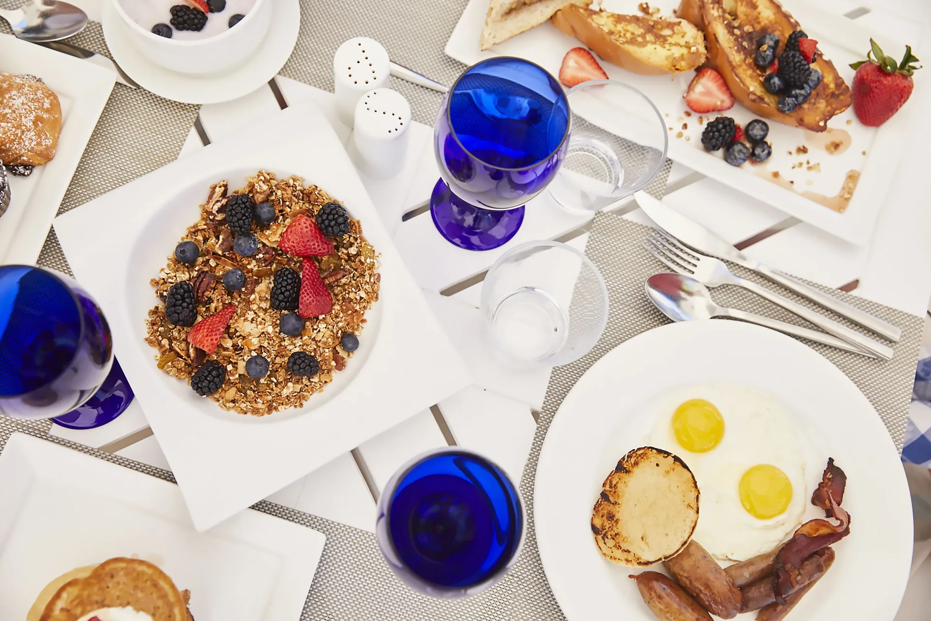 Breakfast plates with fruit, eggs, bacon, and blue glasses at Sandals Royal Curacao.
