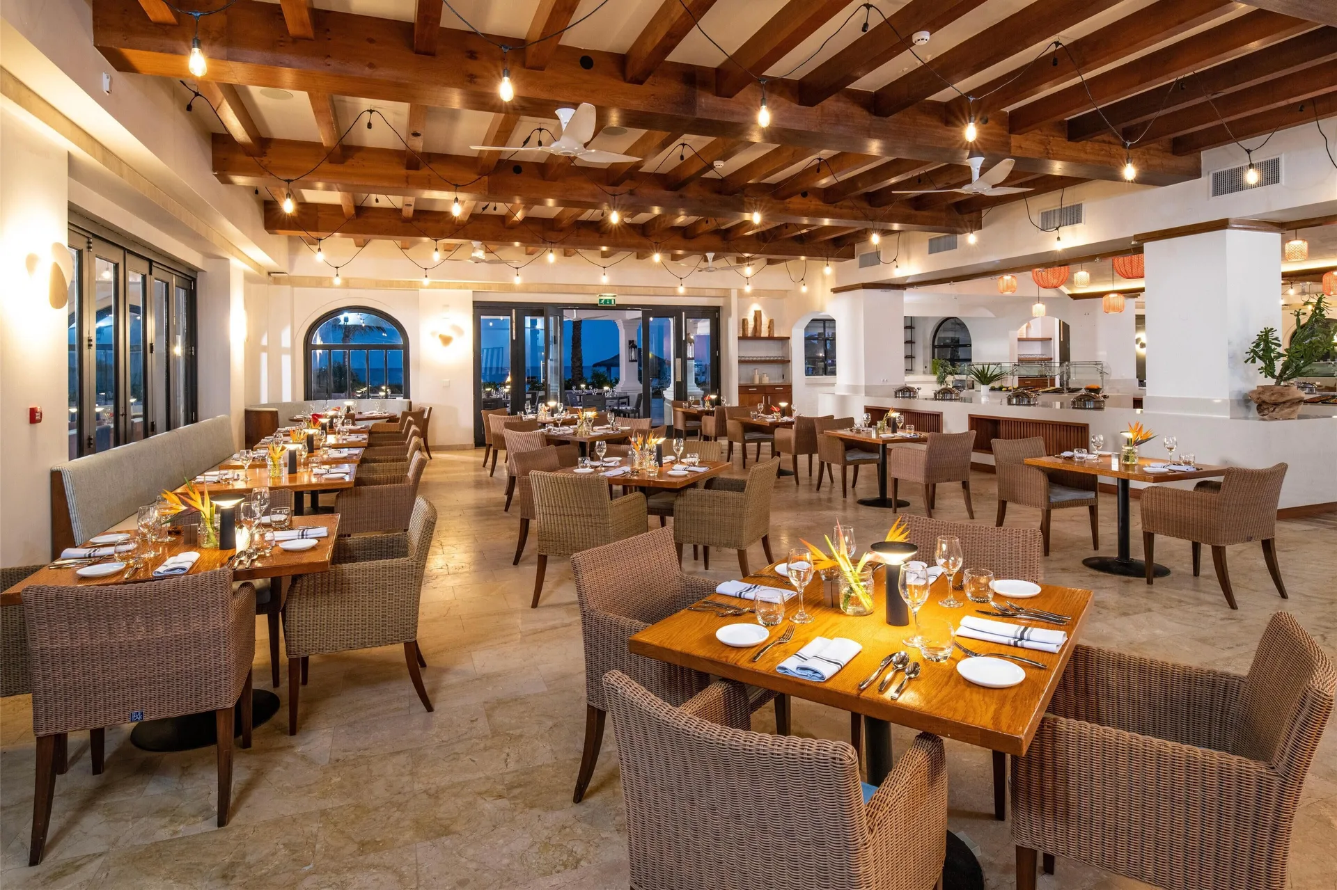 Warm restaurant dining room with wood beams and set tables at Sandals Royal Curacao.