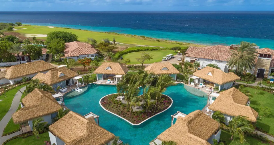 Aerial view of bungalows, island pool, and ocean beyond at Sandals Royal Curacao.