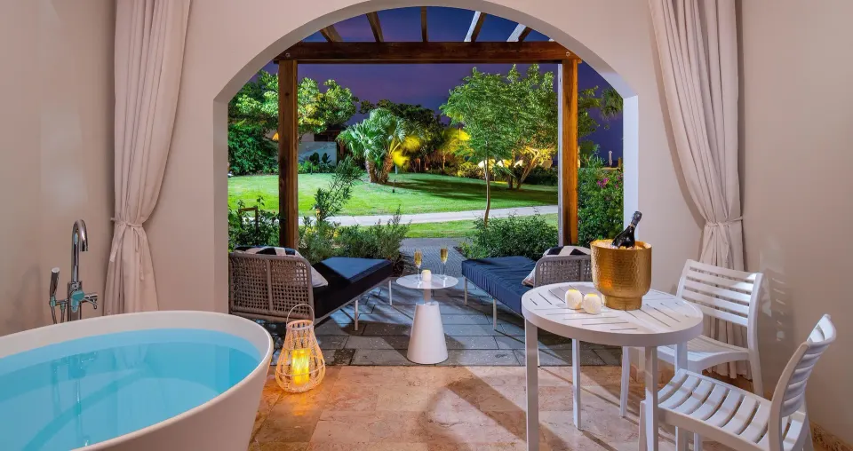 Evening view of junior suite patio soaking tub at Sandals Royal Curacao with loungers and garden lighting.