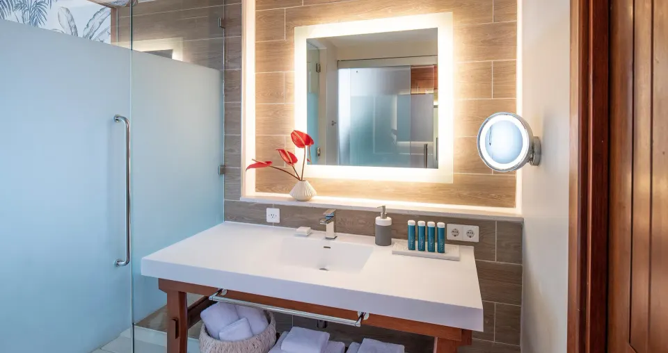 Junior suite bathroom vanity at Sandals Royal Curacao with illuminated mirror and glass shower.