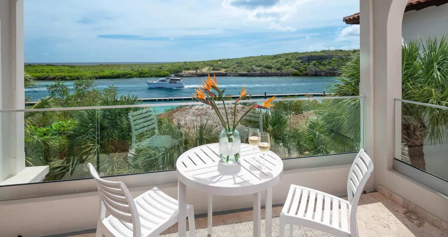 Sunchi Club Level Beachfront Room balcony view at Sandals Royal Curacao with table, chairs, and waterway.