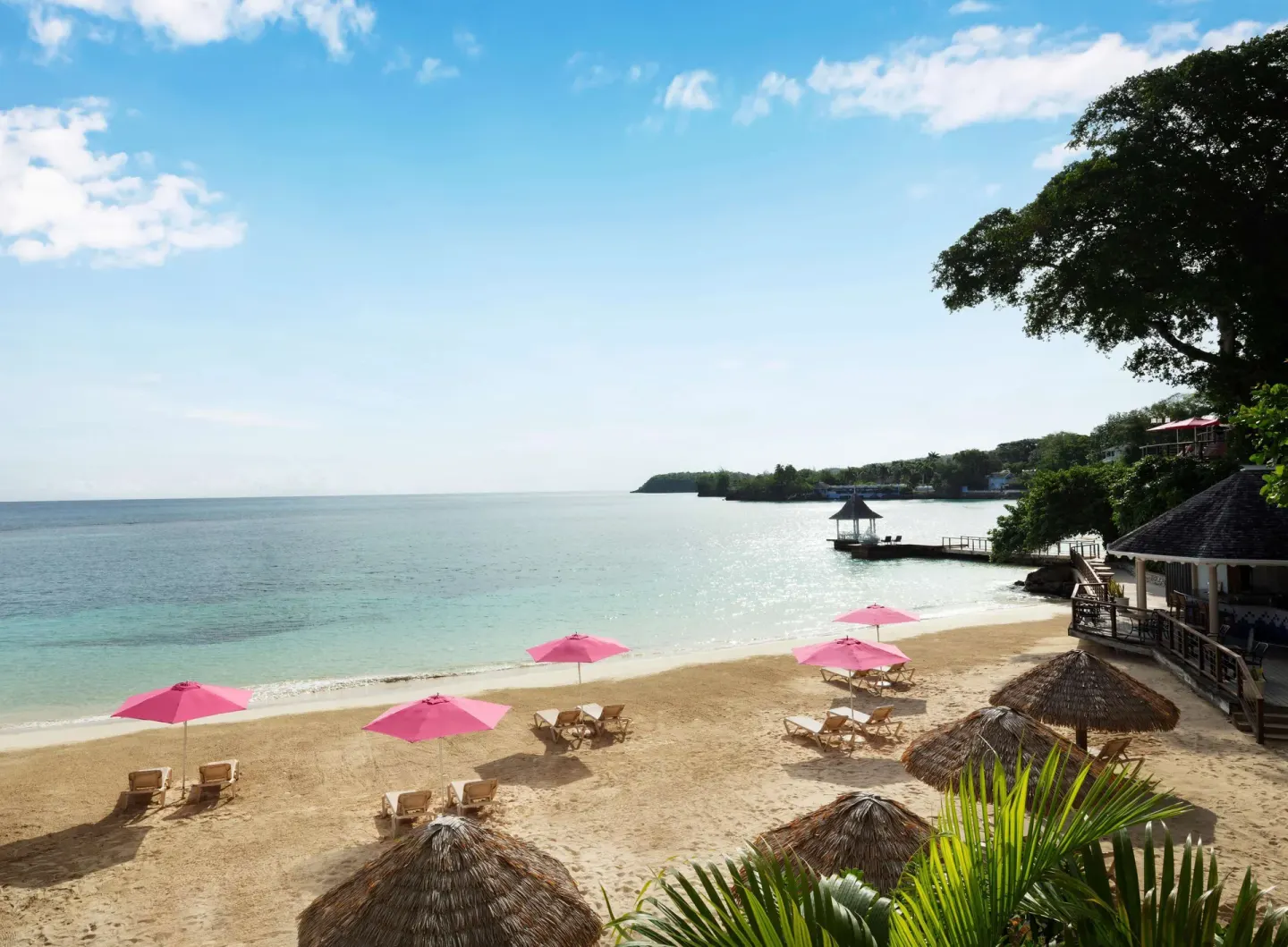 Sandy beach with pink umbrellas and calm water at Sandals Royal Plantation.