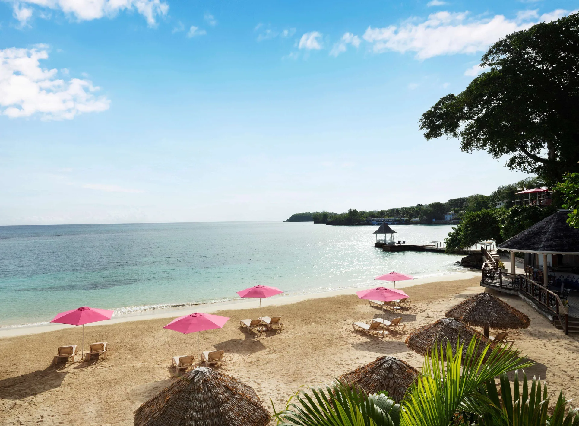 Sandy beach with pink umbrellas and calm water at Sandals Royal Plantation.