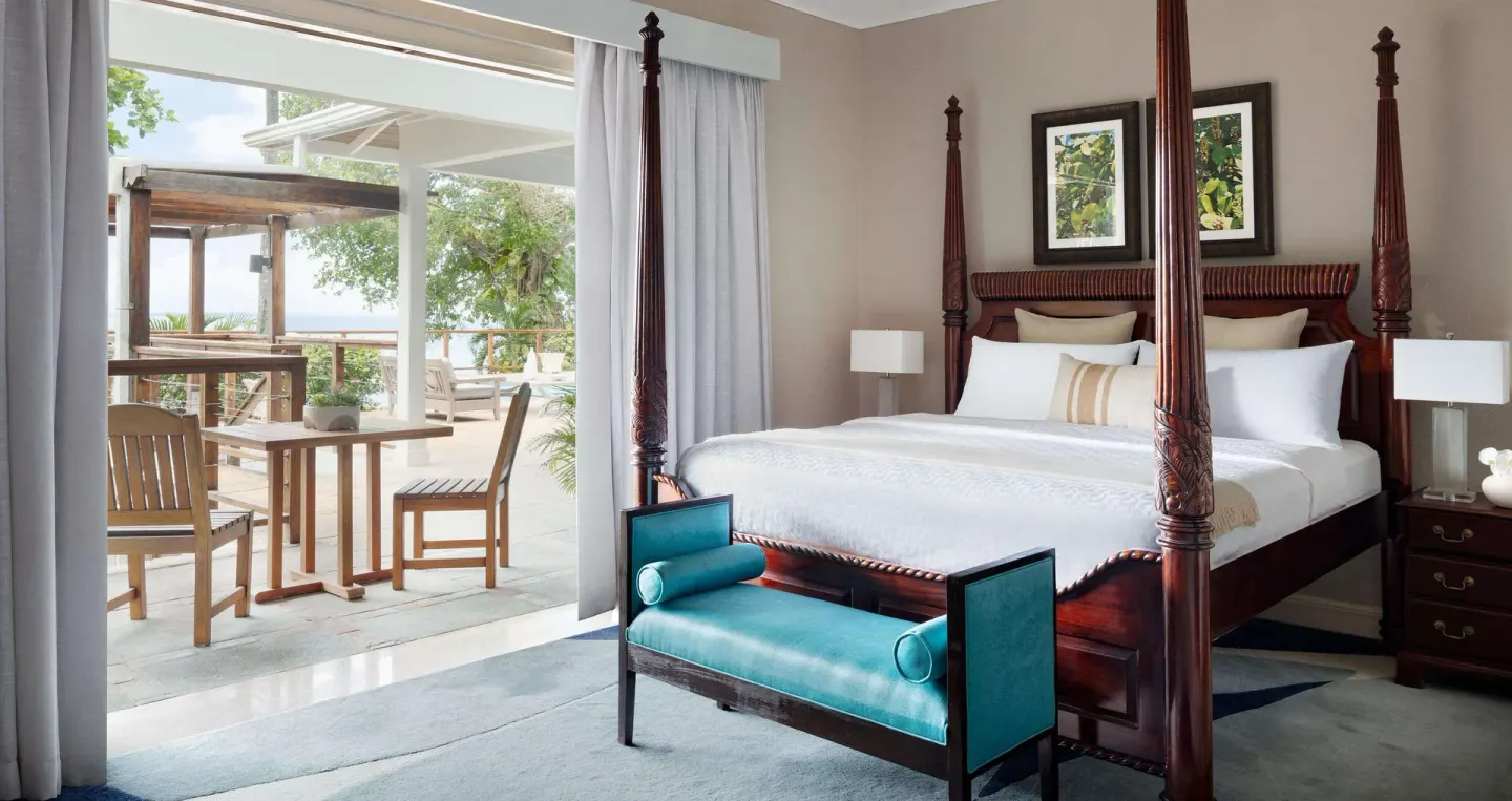 Four-poster king bed and patio seating in a guest room at Sandals Royal Plantation.