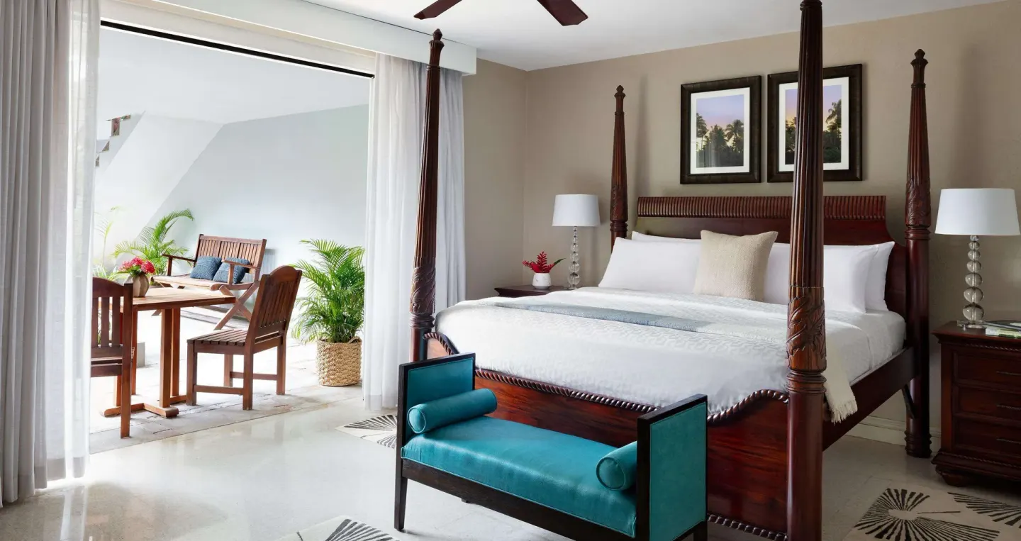 Guest room with four-poster king bed and patio dining set at Sandals Royal Plantation.