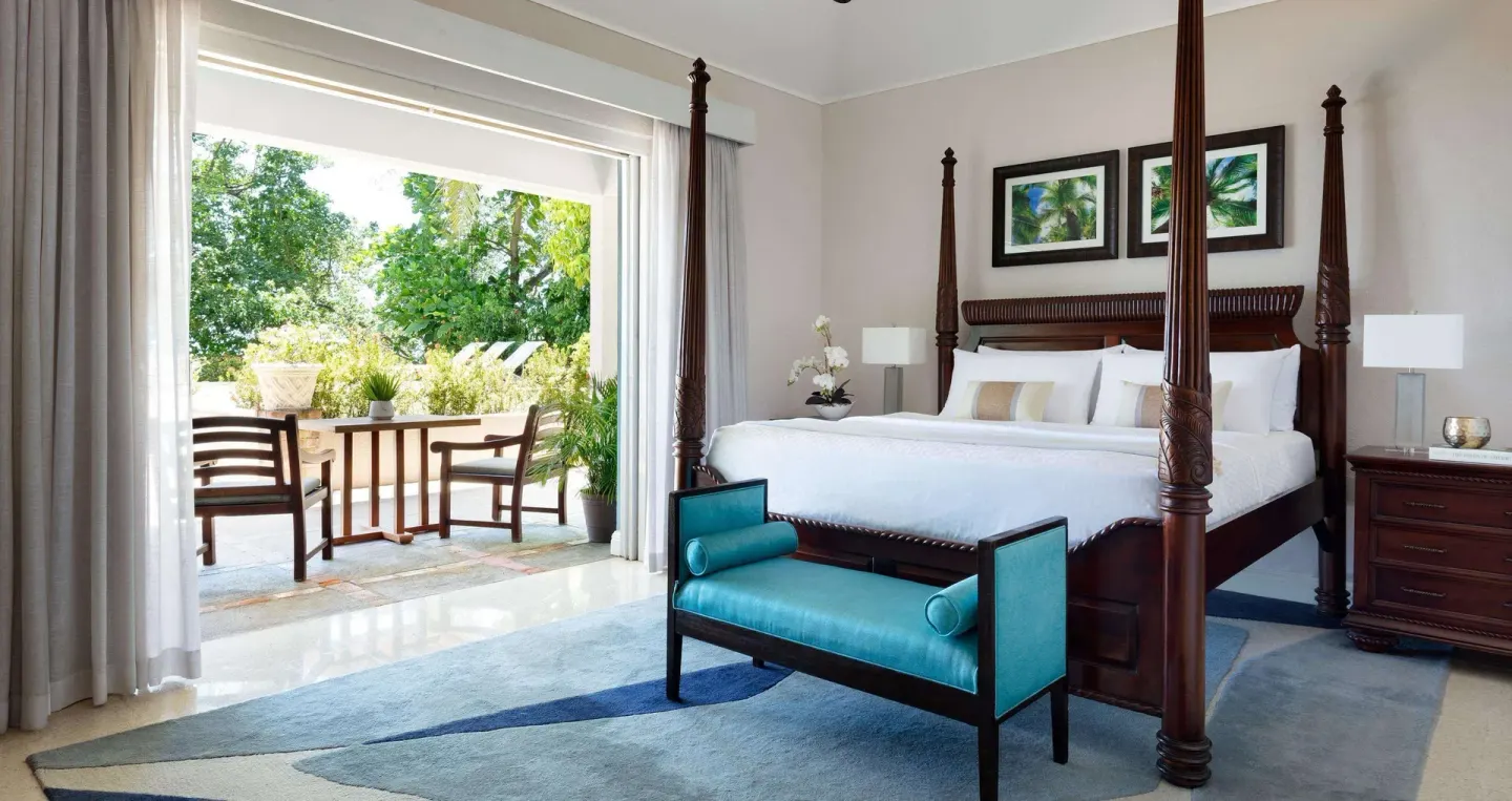 Four-poster king bed beside a leafy terrace in a guest room at Sandals Royal Plantation.