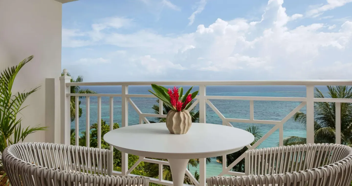 Ocean-view balcony with round table and woven chairs at Sandals Royal Plantation.