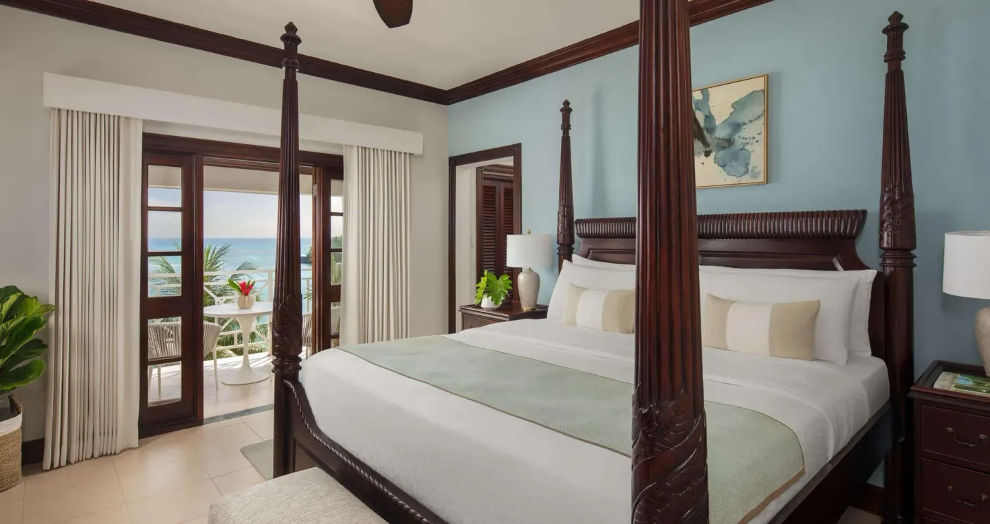 Four-poster king bed at Sandals Royal Plantation with blue accent wall and balcony view.