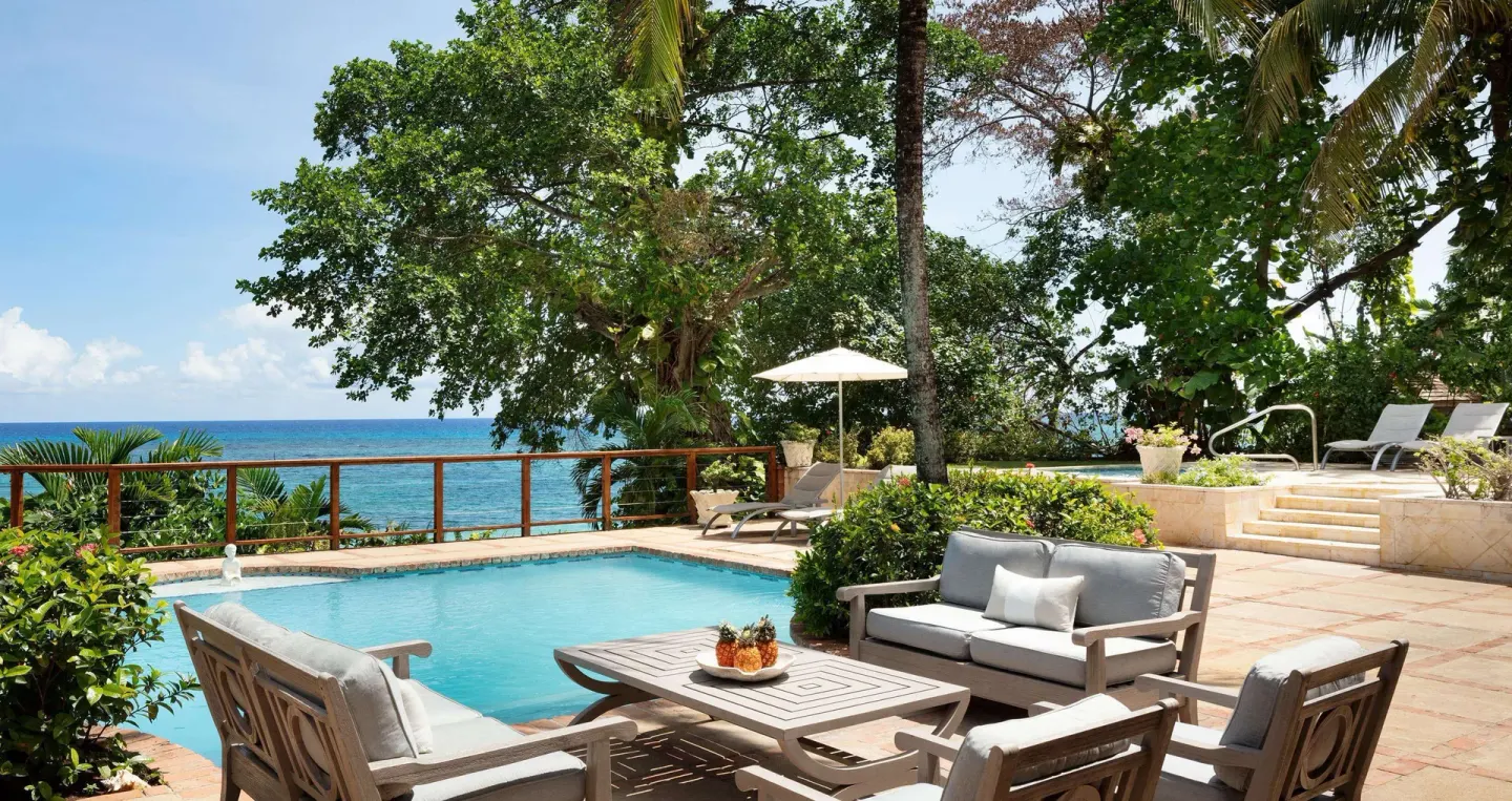 Poolside seating area with ocean beyond the railing at Sandals Royal Plantation.