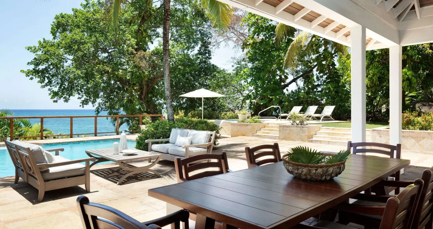 Covered patio dining table beside the pool and ocean at Sandals Royal Plantation.