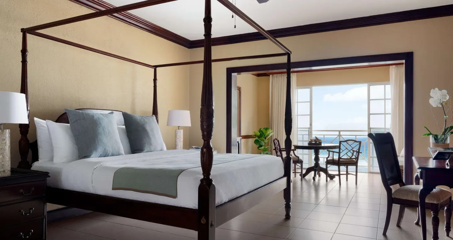 Four-poster bed in a Royal Suite bedroom at Sandals Royal Plantation with ocean visible beyond.