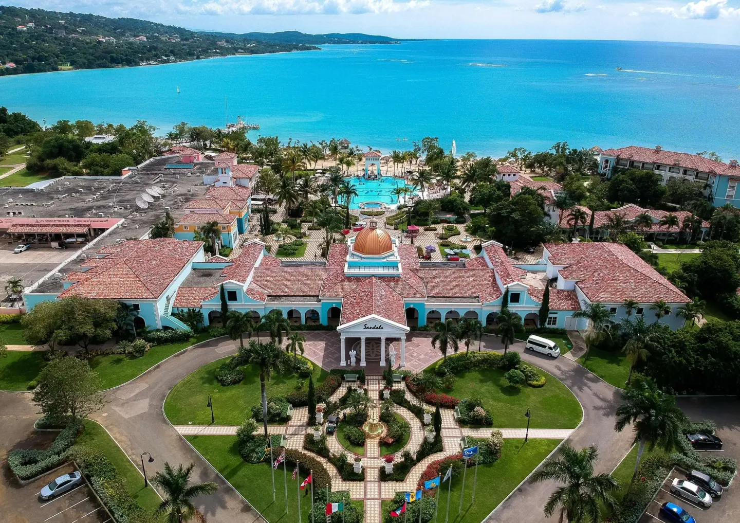 Aerial view of the resort entrance, pool, beach, and blue bay at Sandals South Coast.