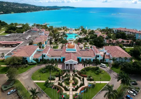 Aerial view of the resort entrance, pool, beach, and blue bay at Sandals South Coast.