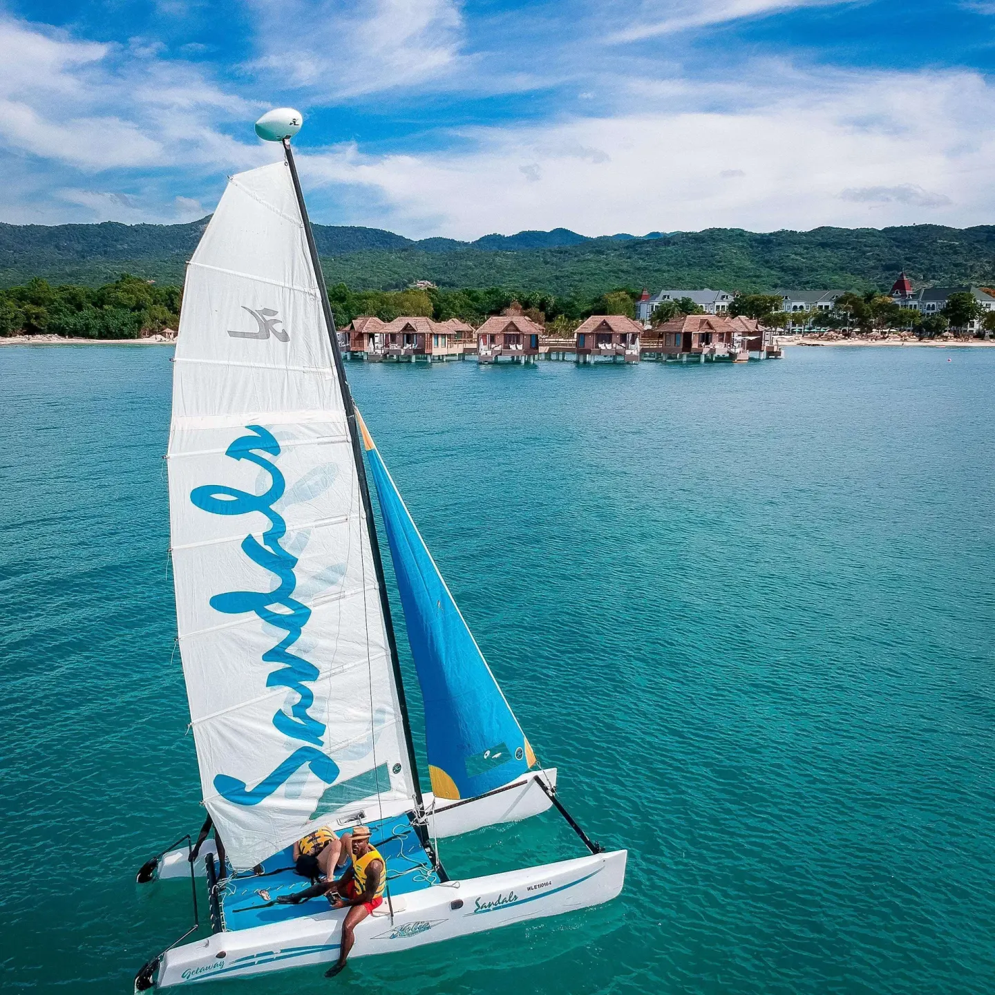Catamaran sailing on turquoise water near overwater bungalows at Sandals South Coast.