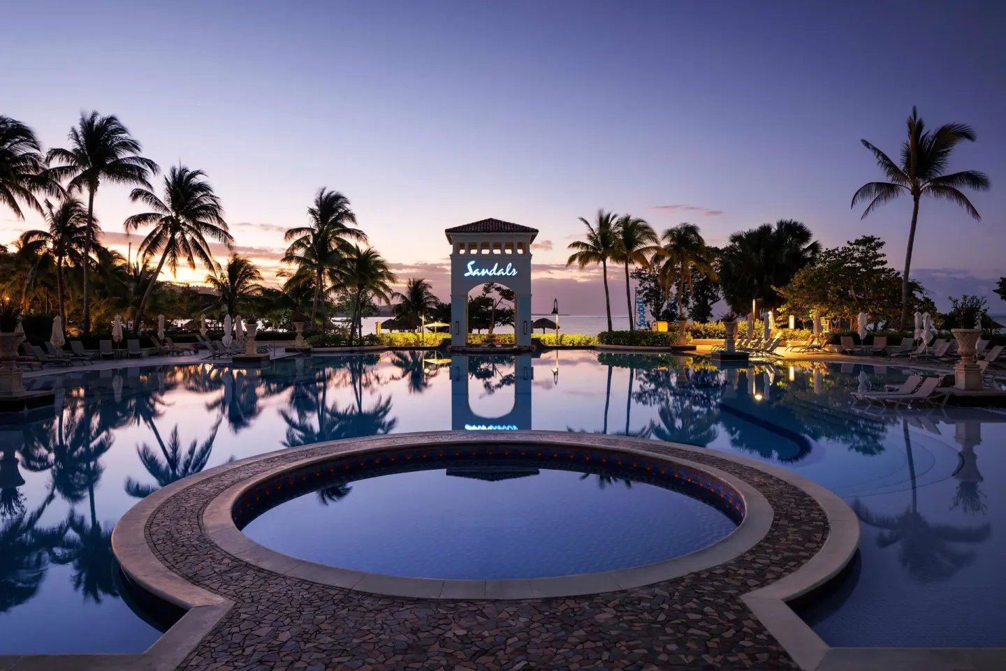 Main pool at dusk with palm silhouettes and arch at Sandals South Coast.