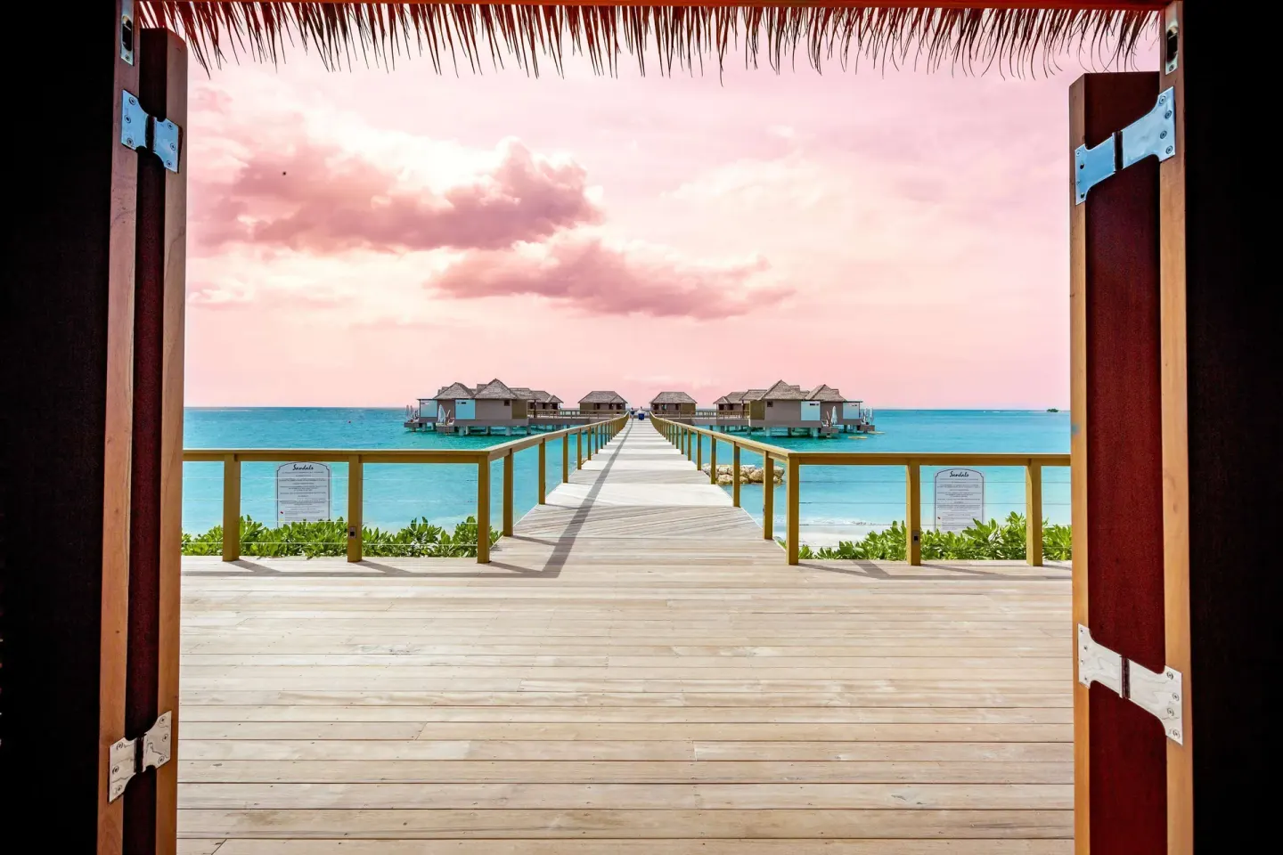 Open wooden doors frame an overwater villa pier and turquoise sea at Sandals South Coast.