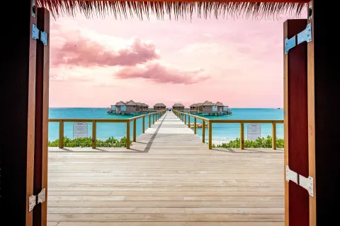 Open wooden doors frame an overwater villa pier and turquoise sea at Sandals South Coast.